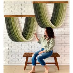 a woman is sitting on a bench in front of some drapes hanging from the wall