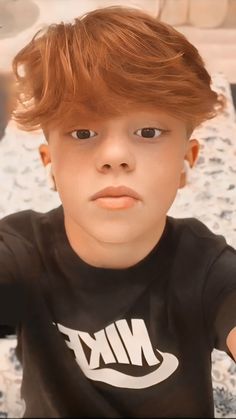 a young boy with red hair wearing a nike t - shirt and looking at the camera