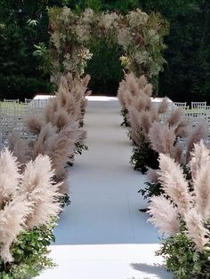 an outdoor ceremony with white chairs and tall pink flowers on the aisle, surrounded by greenery