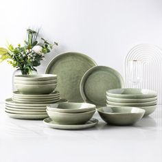 a white table topped with lots of green plates and bowls next to a vase filled with flowers