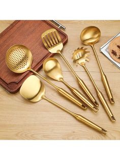 gold colored kitchen utensils on a wooden cutting board and serving tray with spoons