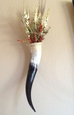 a vase with flowers in it is hanging on the wall next to a hook that has an animal's tail sticking out of it