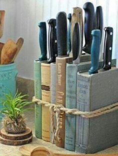 there are many knives in the holder on the table next to books and a potted plant