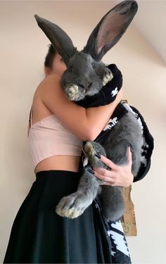 a woman holding a stuffed rabbit in her arms while wearing a skirt and crop top