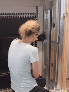 a woman in white shirt and black gloves working on a wall mounted oven with glass doors