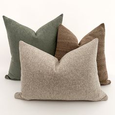 three pillows sitting on top of each other in different colors and sizes, one is brown, the other is green