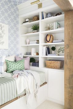 a white book shelf filled with books next to a bed and pillows on top of it