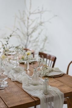 a wooden table topped with lots of white flowers and vases filled with small white flowers