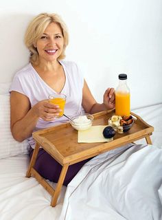 a woman sitting on a bed holding a tray with orange juice and yogurt