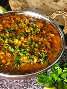 a large metal bowl filled with food next to some bread and cilantro leaves