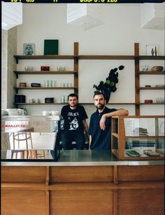 two men sitting at a counter in a coffee shop, one is leaning on the counter