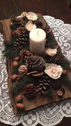 a wooden tray with pine cones, candles and flowers sitting on top of a doily