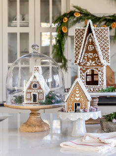 two gingerbread houses under a glass dome on a kitchen counter with christmas decorations around them