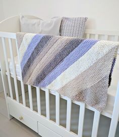 a white crib with a blue and gray blanket on it's bottom shelf