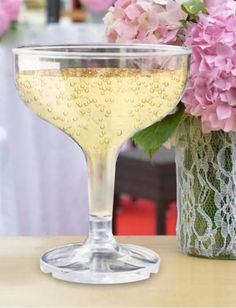 a glass filled with liquid sitting on top of a wooden table next to pink flowers