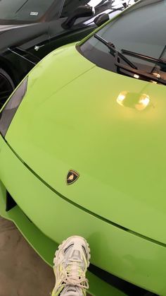 a green sports car parked in a garage next to another vehicle with its hood up