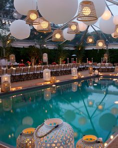 an outdoor swimming pool with lanterns hanging from the ceiling and tables set up around it