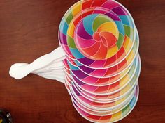 a stack of colorful paper plates sitting on top of a wooden table next to a cup