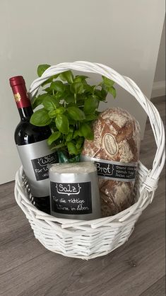 a white basket filled with bread and bottles of wine next to a potted plant