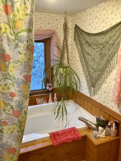 a bath tub sitting under a window next to a wooden shelf with potted plants