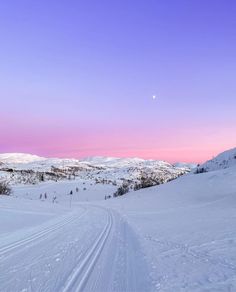 there is a pink sky over the snow covered mountains and road that leads to it