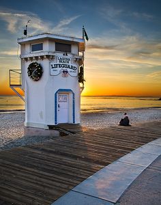 a lifeguard tower sitting on top of a wooden pier next to the ocean at sunset