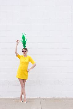 a woman in a yellow dress with a green pineapple on her head and sunglasses