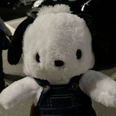 a white teddy bear with black eyes and overalls on it's chest, sitting in front of a car