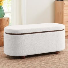 a white ottoman sitting on top of a carpeted floor next to a vase with yellow flowers