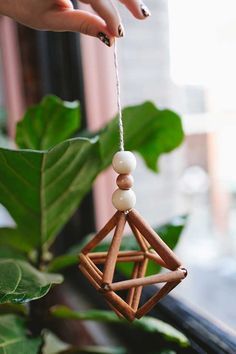 a hand holding a wooden ornament hanging from a window sill next to a plant