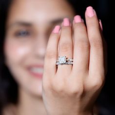 a woman with pink nail polish holding her engagement ring in front of her face and smiling at the camera