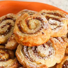 cinnamon rolls piled on top of each other in an orange bowl with powdered sugar