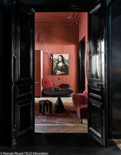 an open door leading to a living room with pink walls and black furniture in it