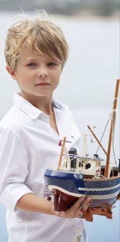 a young boy holding a model boat in his hands