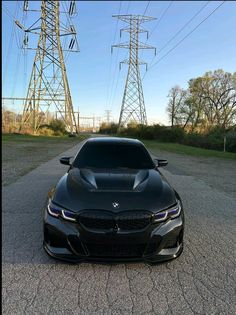 the front end of a black car parked in a parking lot next to power lines