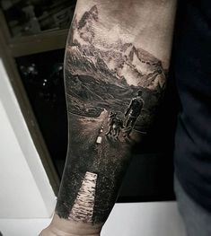 a man's arm with a mountain scene on it and a person walking down the road