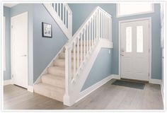 a white stair case next to a door in a blue room with light wood floors