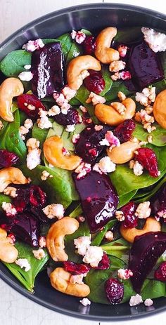 a salad with beets, walnuts and spinach in a black bowl on a white table