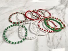 six bracelets with green, red and white beads on a marble countertop next to each other