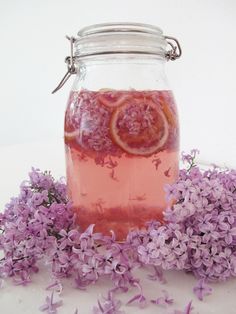 a glass jar filled with liquid next to purple flowers and lemon slices on a white surface