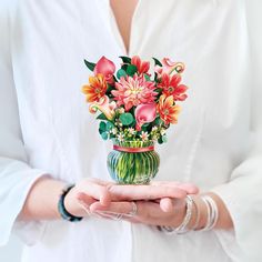 a woman holding a vase filled with flowers on top of her hands and wearing bracelets