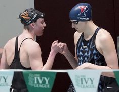 two young men standing next to each other wearing swimming caps and holding hands in front of them