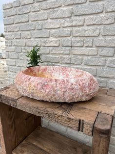 a stone bowl sitting on top of a wooden table next to a brick wall with a plant in it