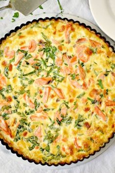 a quiche with salmon and spinach in a pie pan next to a plate