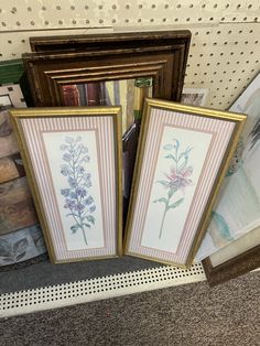 two framed pictures sitting on top of a floor next to a pile of books and magazines