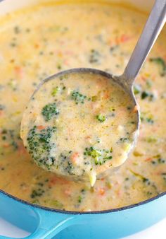 a ladle filled with broccoli and cheese soup in a blue pot on top of a table