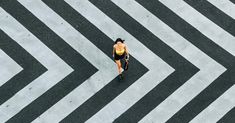 an aerial view of a woman walking across a street with black and white stripes on the ground