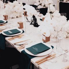 the table is set with white flowers and green napkins, gold place settings and wooden utensils