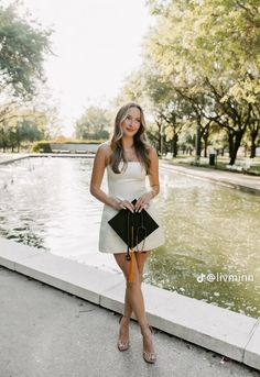 a beautiful young woman standing next to a pond holding an orange and black purse in her hand