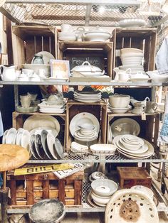 a man standing in front of a shelf filled with dishes and pans on top of wooden crates